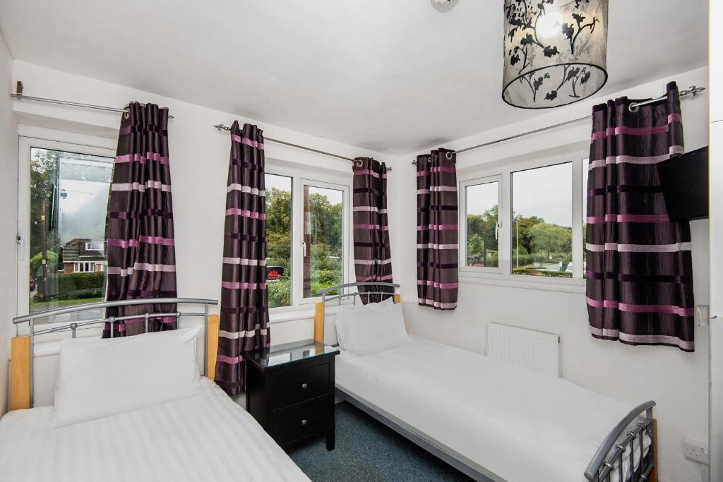two beds in a room with two windows at Chris's Motel in Stokenchurch