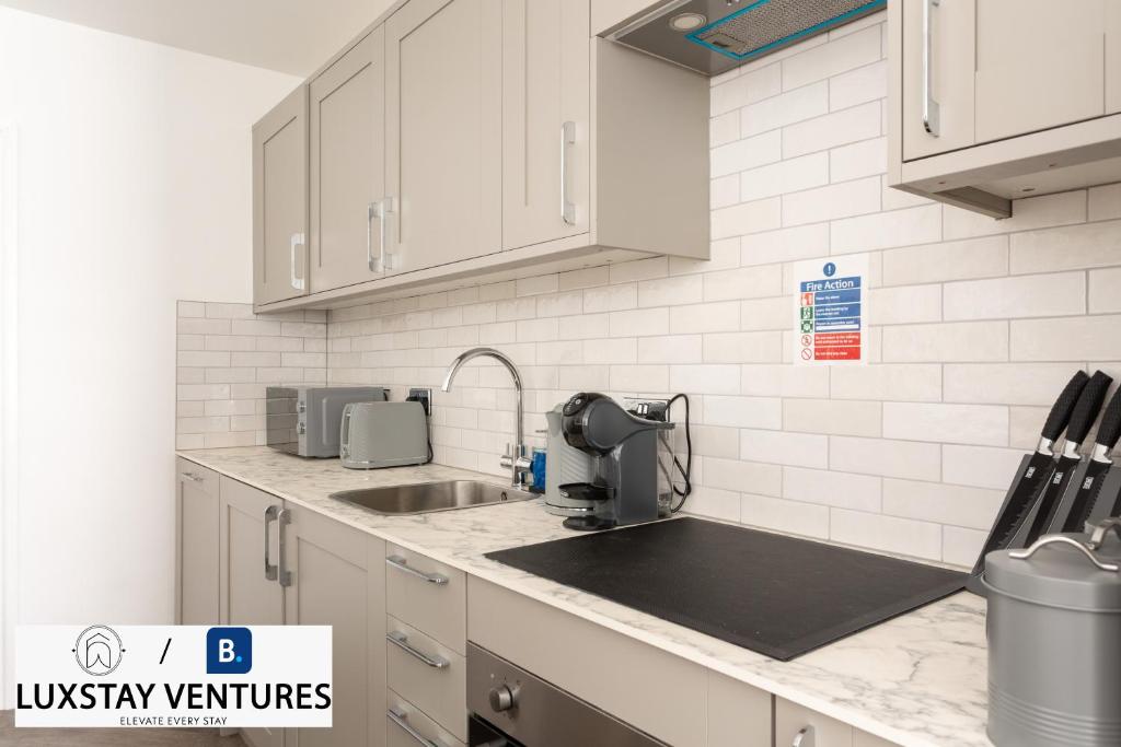 a kitchen with white cabinets and a sink with a mixer at Bright and Spacious 2BR Maisonette Sleeps 8, Game Room, 5 mins to Brighton Beach and City Centre in Brighton & Hove