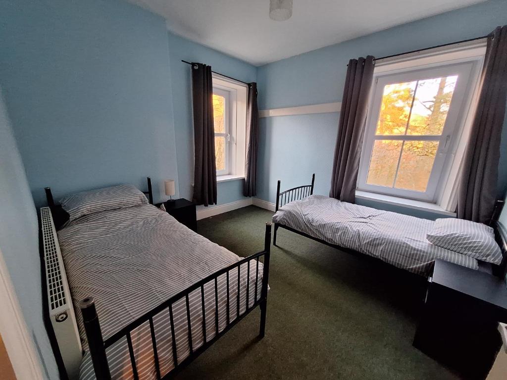 a bedroom with two beds and two windows at Carlcroft Cottage in Alwinton