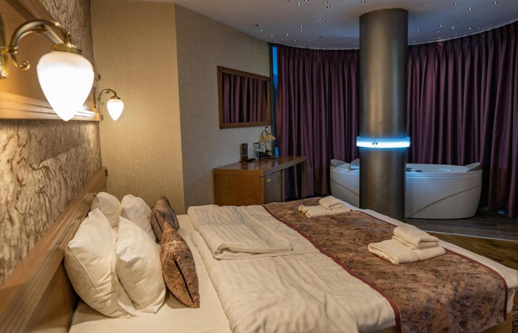 Double bed with decorative pillows, bedside lamp and desk, plus a purple-curtained whirlpool tub with blue LED column at City Palace Hotel in Ohrid