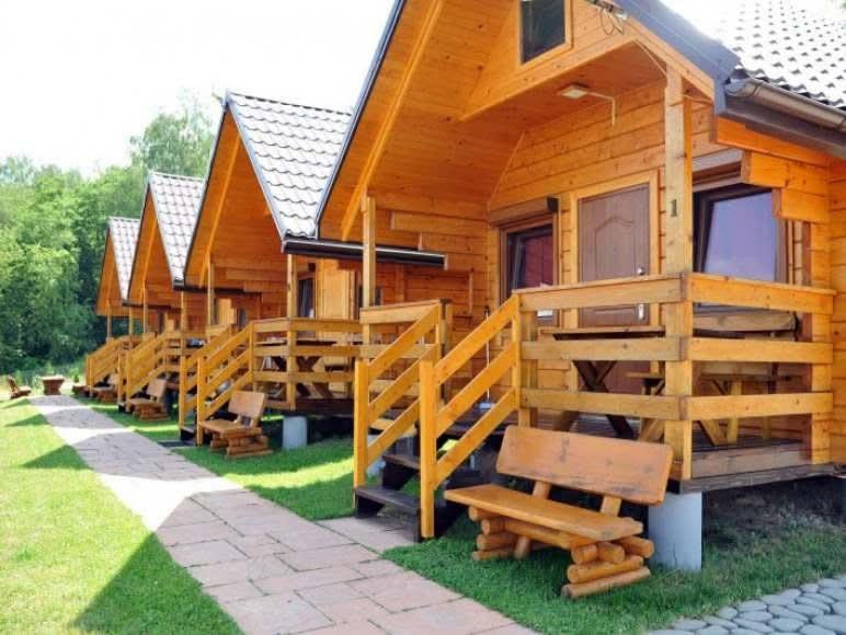 a row of wooden lodges with benches in the grass at Domki PIĘKNY WIDOK górne - Solina Centrum in Solina