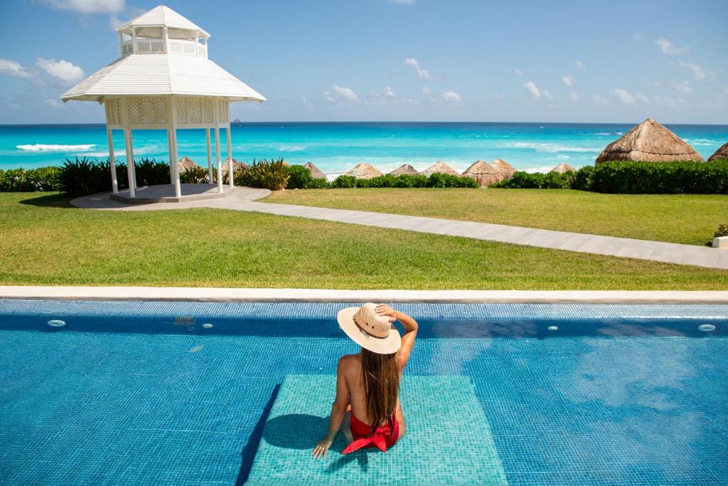a woman in a hat sitting next to a swimming pool at Paradisus Cancun All Inclusive in Cancún