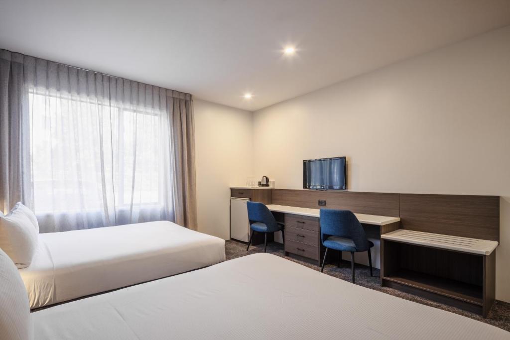 a hotel room with two beds and a desk at Heartland Hotel Auckland Airport in Auckland