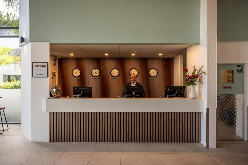 an office with clocks on the wall and a man sitting at a counter at Heartland Hotel Auckland Airport in Auckland