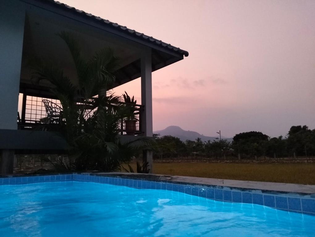 a swimming pool in front of a house with the sunset at Baksaei Retreat Ricefield Villas in Kampot