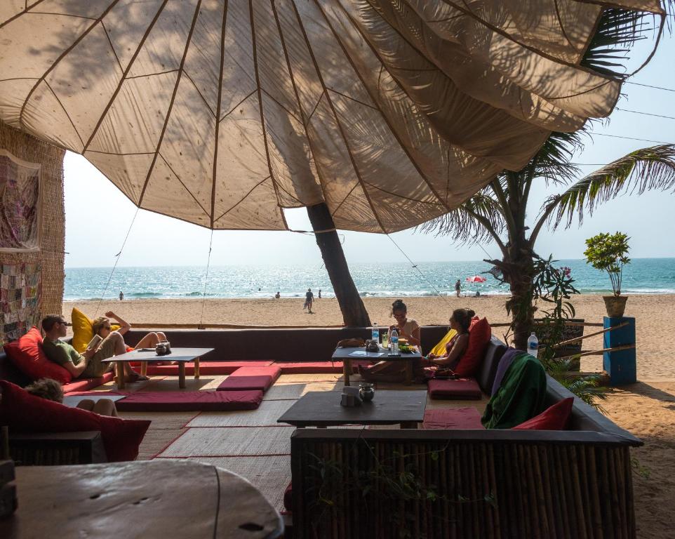 a group of people sitting under an umbrella on the beach at Jardim a Mar in Agonda