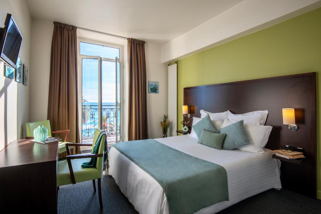 a hotel room with a bed and a desk and a window at Hôtel Vendôme Menton in Menton