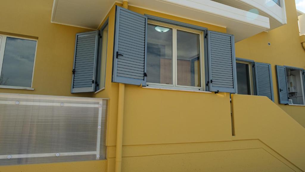 a house with blue shutters on a yellow wall at Smart and Sea in Tortoreto Lido