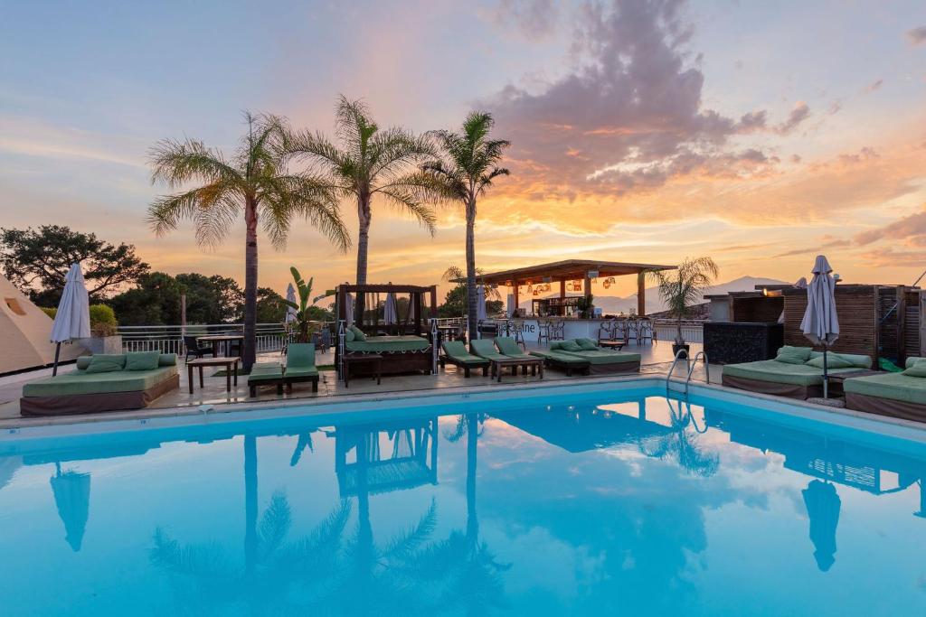 a swimming pool with palm trees and a sunset at Bella Vista Hôtel, Spa & Gastronomie in Porticcio