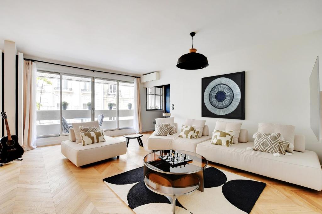 un salon avec des meubles blancs et une grande fenêtre dans l'établissement Magnifique appartement 140 m2 avec terrasse - bail mobilité, à Paris