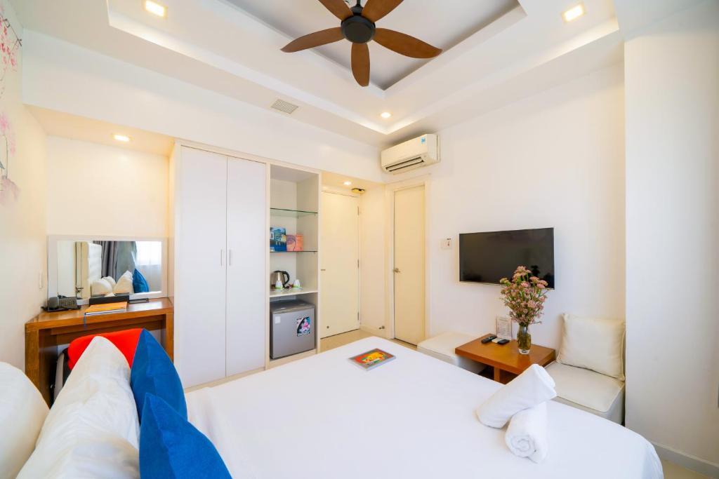 A bedroom arranged around a white bed, television, armchair and compact refreshment station.