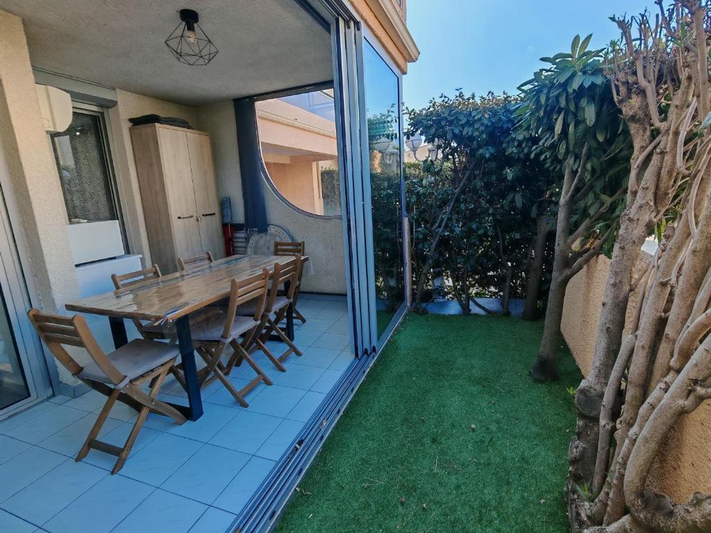 une table et des chaises en bois sur une terrasse avec pelouse dans l'établissement Appartement moderne 2 chambres, proche plage et parking privatif - FR-1-732-104, à Argelès-sur-Mer