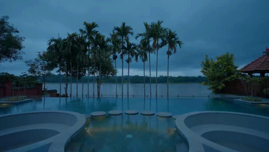 una piscina con vistas al agua y a las palmeras en The River Retreat Heritage Ayurvedic Resort, en Shoranūr