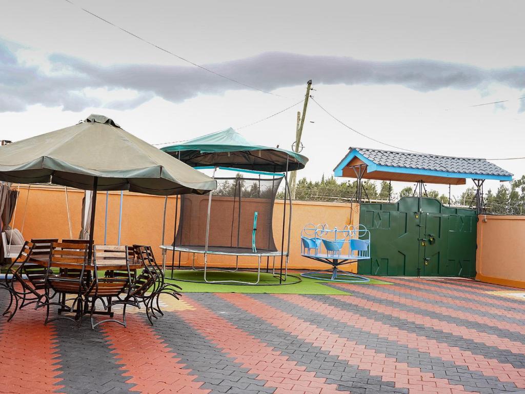 un patio avec tables et chaises avec parasols et une aire de jeux dans l'établissement Happy Trails Home- Nanyuki, à Nanyuki