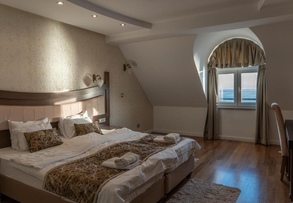 Attic double room with sloped ceiling, arched window with sea view, bedside sconces, hardwood floors and folded towels at City Palace Hotel in Ohrid
