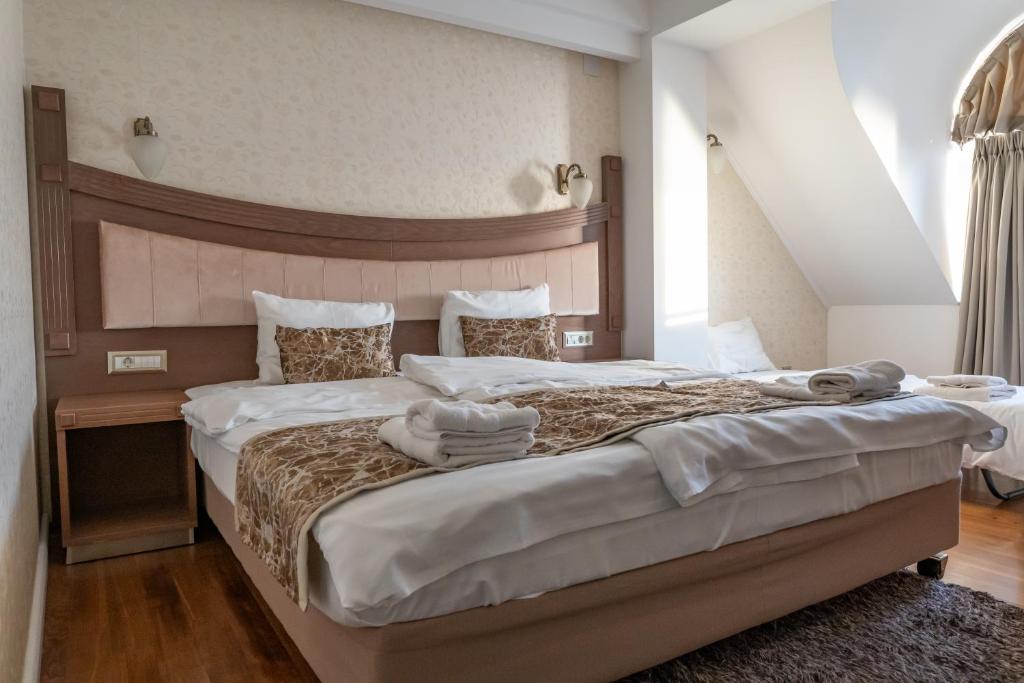 Double bed with upholstered headboard, bedside table, wall sconces, folded towels and rolled linens, adjacent single bed at City Palace Hotel in Ohrid