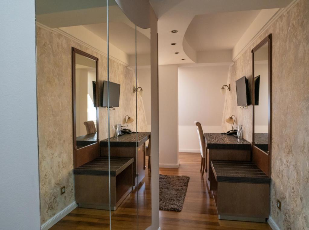 Guest room with wall-mounted TV, two long work desks with lamps and mirrors, bench seating, hardwood floors and area rug at City Palace Hotel in Ohrid