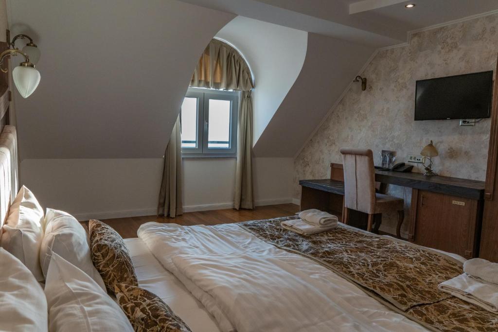 Attic double room with sloped ceiling, patterned wallpaper, wall-mounted TV, desk, window with curtains and folded towels at City Palace Hotel in Ohrid