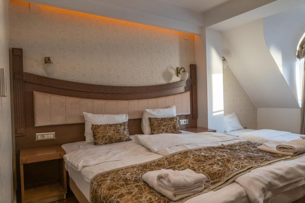 Attic double room with sloped ceiling, wooden headboard, bedside lamps, wall sconces, folded towels on bed and mirror at City Palace Hotel in Ohrid