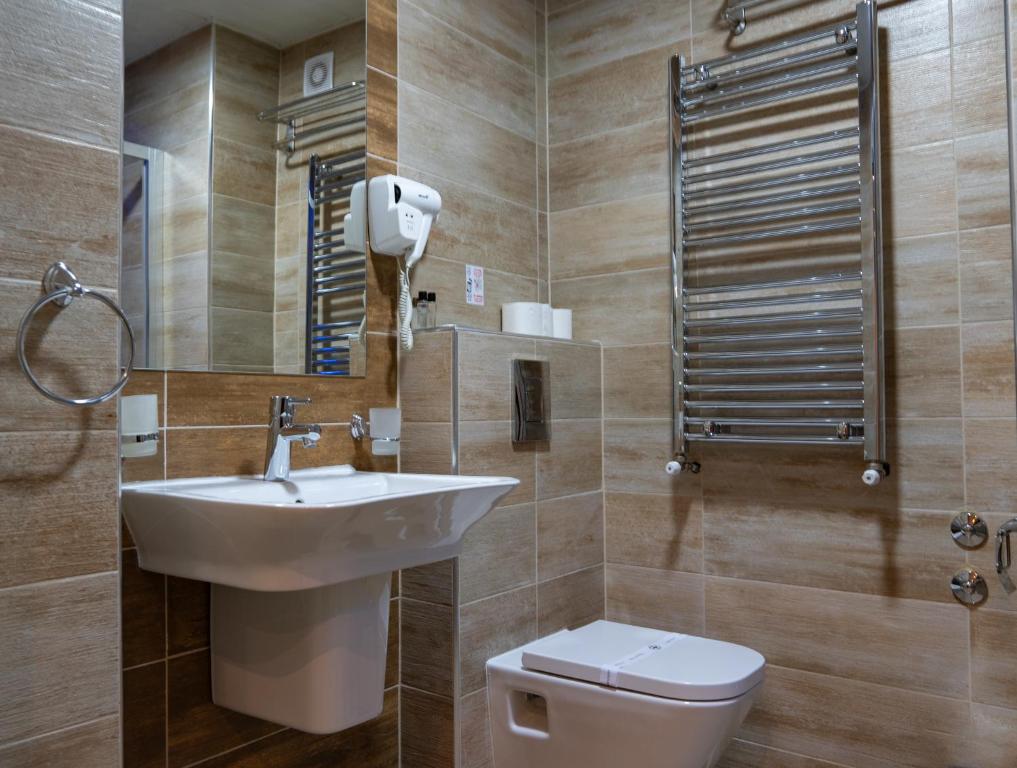 Bathroom with wall-mounted hairdryer, heated towel rail, sink, toilet and mirror with soap dispenser and ring at City Palace Hotel in Ohrid