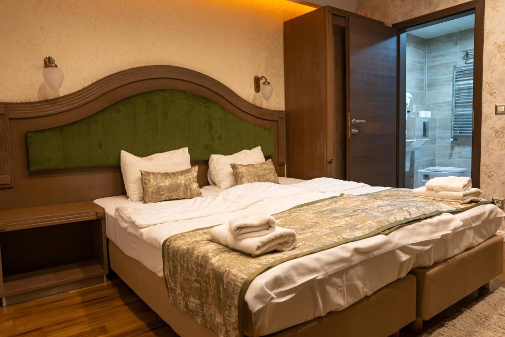 Double bed with green upholstered headboard, bedside sconce, folded towels and en-suite bathroom with heated towel rail at City Palace Hotel in Ohrid
