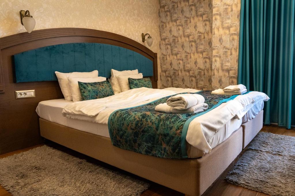 Double bed with teal upholstered headboard, patterned runner and pillows, folded towels, wall sconce and patterned wallpaper at City Palace Hotel in Ohrid