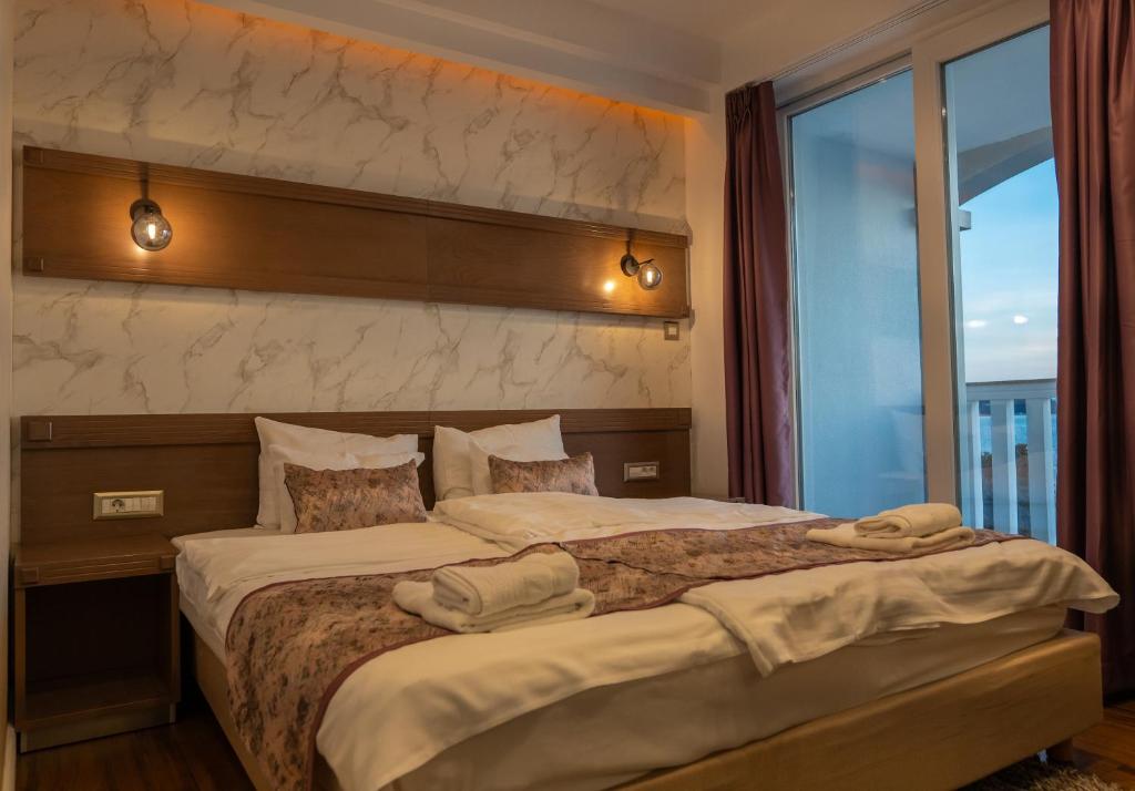 Double bed with folded towels, patterned runner and pillows, marble-effect accent wall, bedside lights and balcony access at City Palace Hotel in Ohrid
