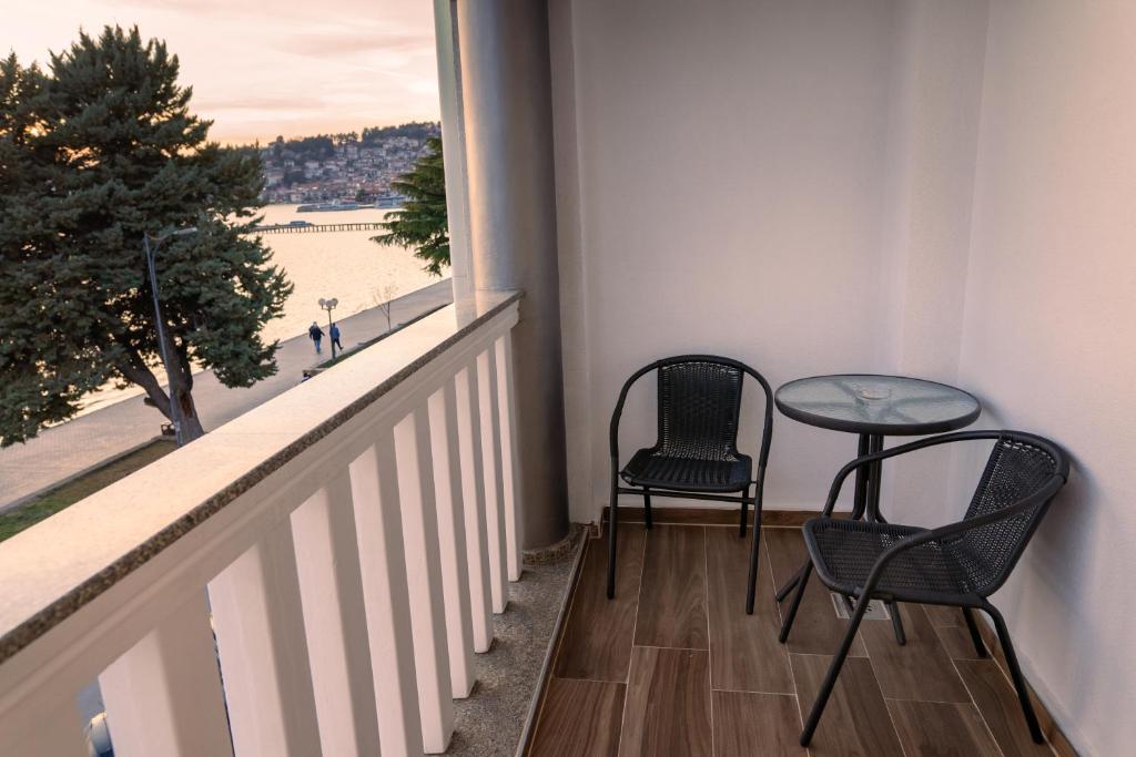 Private balcony with two wicker chairs, round glass-top table and wood-look flooring overlooking the sea and promenade at City Palace Hotel in Ohrid