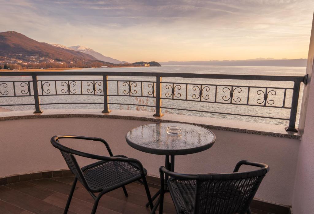 Balcony with two wicker chairs, round table and ashtray overlooking lake and mountains at sunset, wrought-iron railing at City Palace Hotel in Ohrid