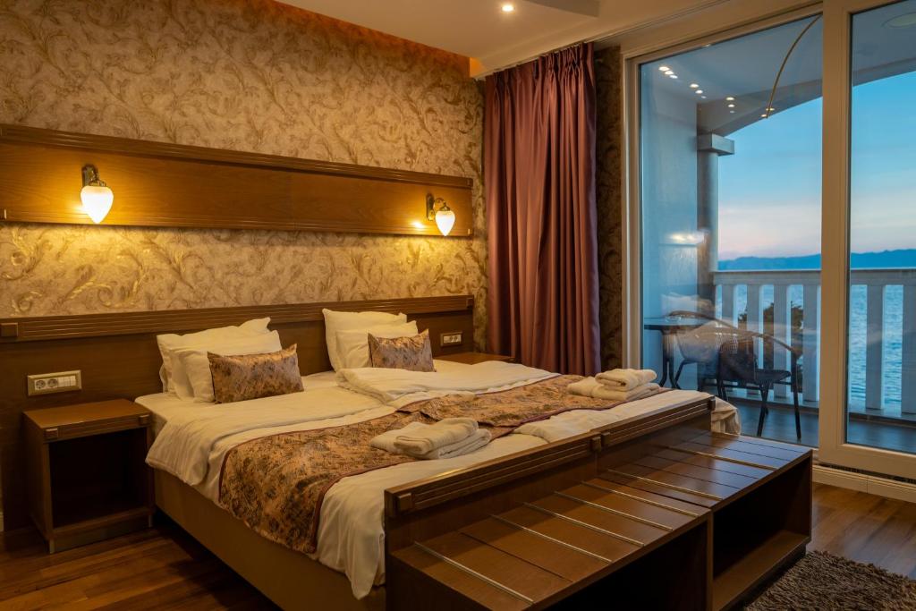 Double bed with patterned runner and towels, bedside lamps, wallpaper accent and sliding glass door to balcony with ocean view at City Palace Hotel in Ohrid