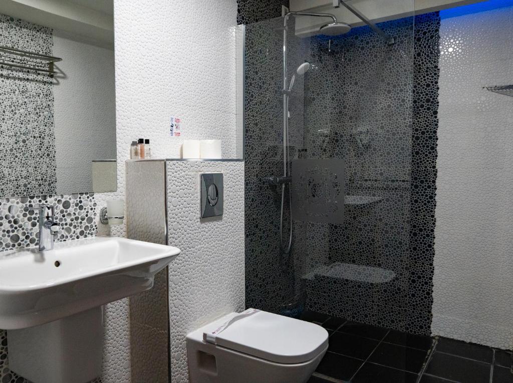 Compact bathroom with patterned tile walls, glass shower with sliding door, wall-mounted sink and toilet, and toiletries at City Palace Hotel in Ohrid