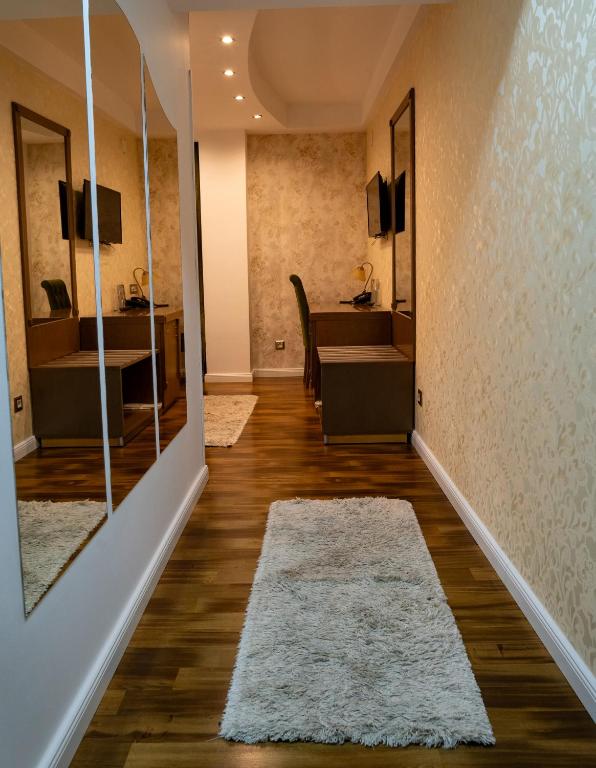 Hallway with hardwood floors, white shag rug, mirrored wardrobe, wall-mounted TV, desk with phone and bench at City Palace Hotel in Ohrid