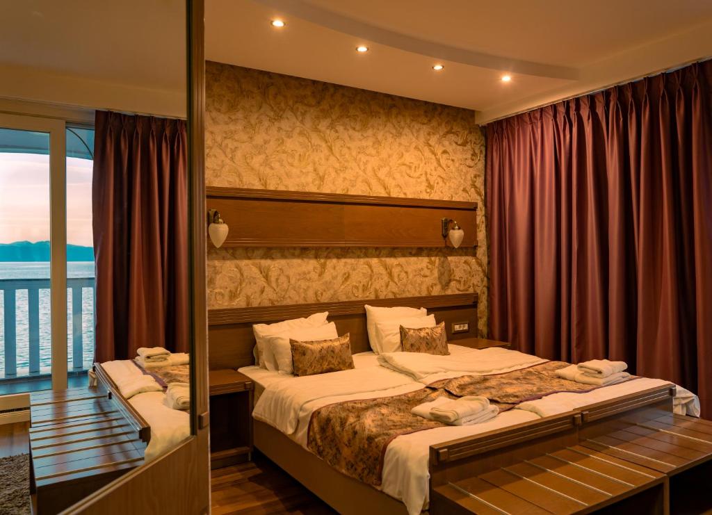 Sea-view room with two beds, patterned wallpaper, wall sconces, bedside shelf, folded towels and balcony doors at City Palace Hotel in Ohrid