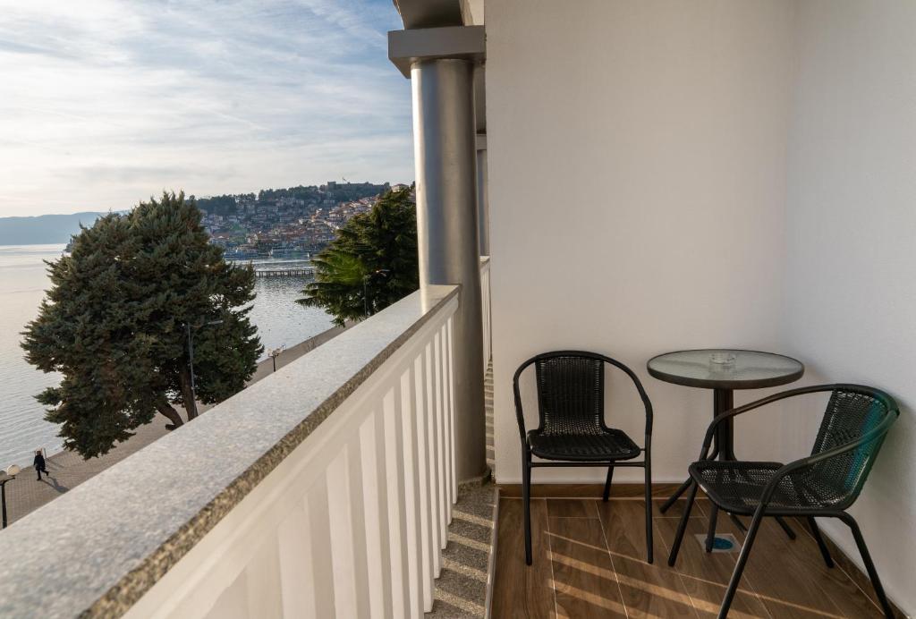Private balcony with two mesh chairs, small table and glass railing overlooking the sea and coastal town at City Palace Hotel in Ohrid