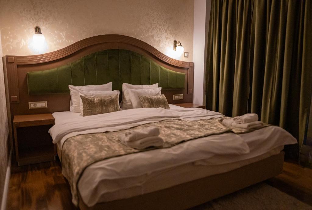 Double bed with green upholstered headboard, wall sconces, bedside tables, folded towels and patterned throw at City Palace Hotel in Ohrid