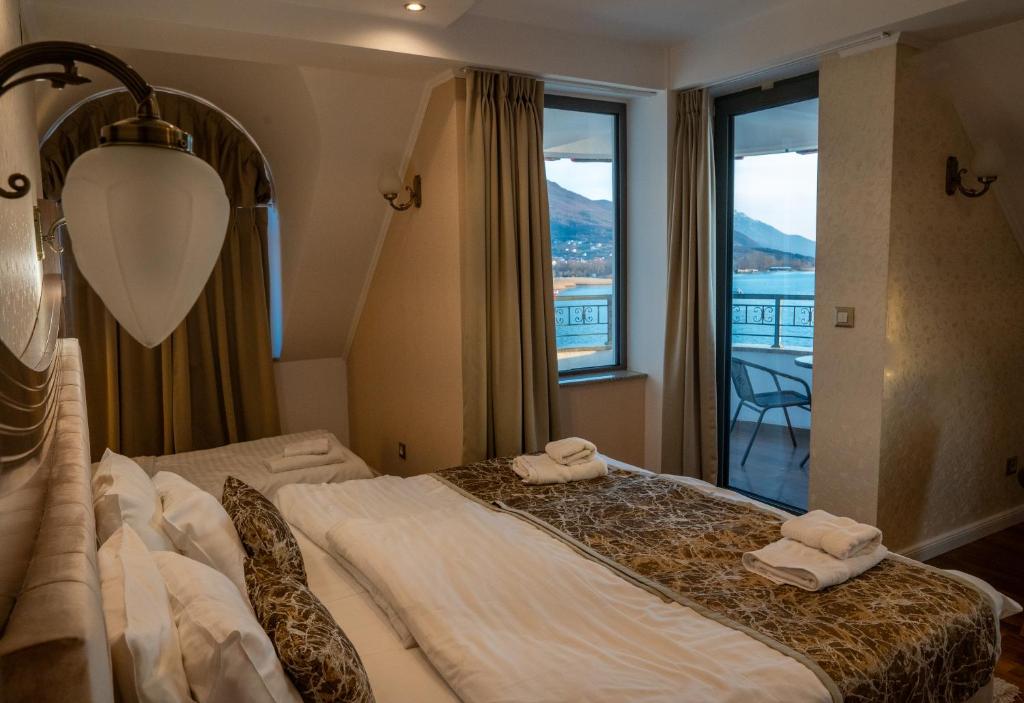 Twin beds with folded towels, bedside lamps and balcony doors with lake view; room labeled 'k' at City Palace Hotel in Ohrid