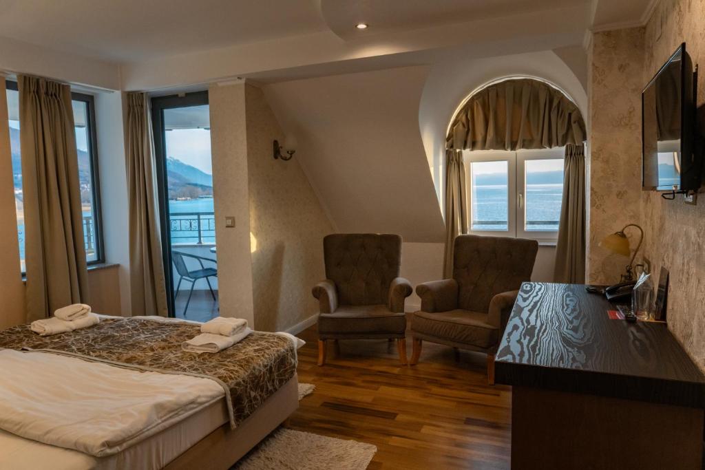 Lake-view room with balcony, wall-mounted TV, desk with patterned lamp, folded towels on bed and two wingback chairs at City Palace Hotel in Ohrid