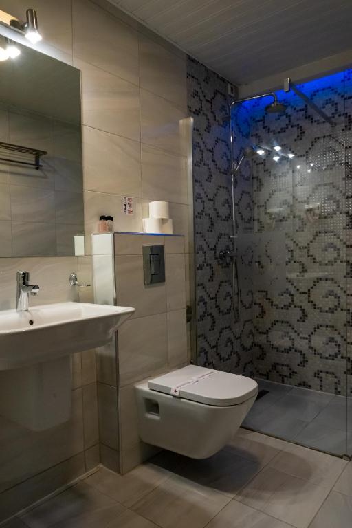 Bathroom with wall-mounted toilet, sink, patterned glass shower with rain head and blue LED lighting at City Palace Hotel in Ohrid