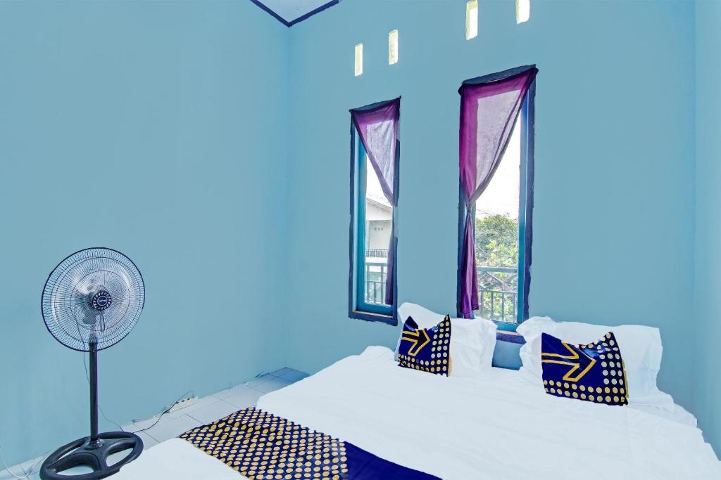 een blauwe kamer met een bed, een ventilator en ramen bij SPOT ON 91918 Najla Guest House Syariah in Parit