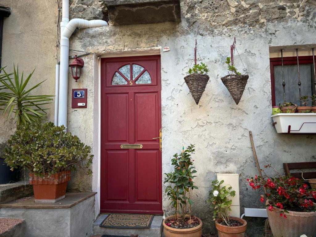 une porte rouge sur le côté d'un bâtiment avec des plantes dans l'établissement village house, à Villeneuve-Loubet