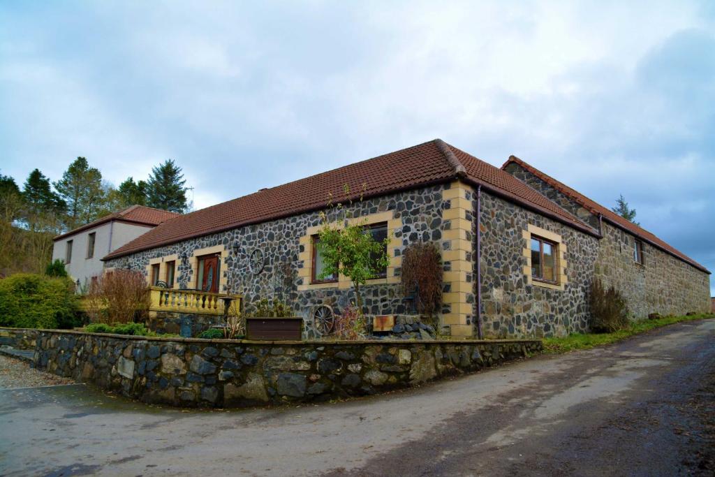 una casa in pietra sul lato di una strada di The Steadings Log Cabins a Kettlebridge