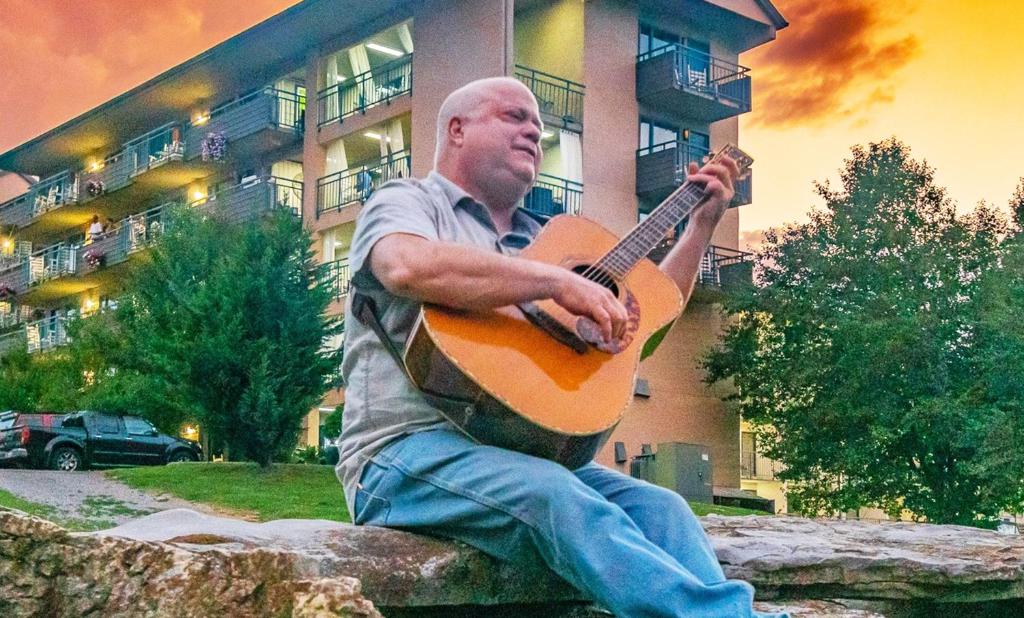 a man sitting on a rock playing a guitar at Arbors at Island Landing Hotel & Suites in Pigeon Forge