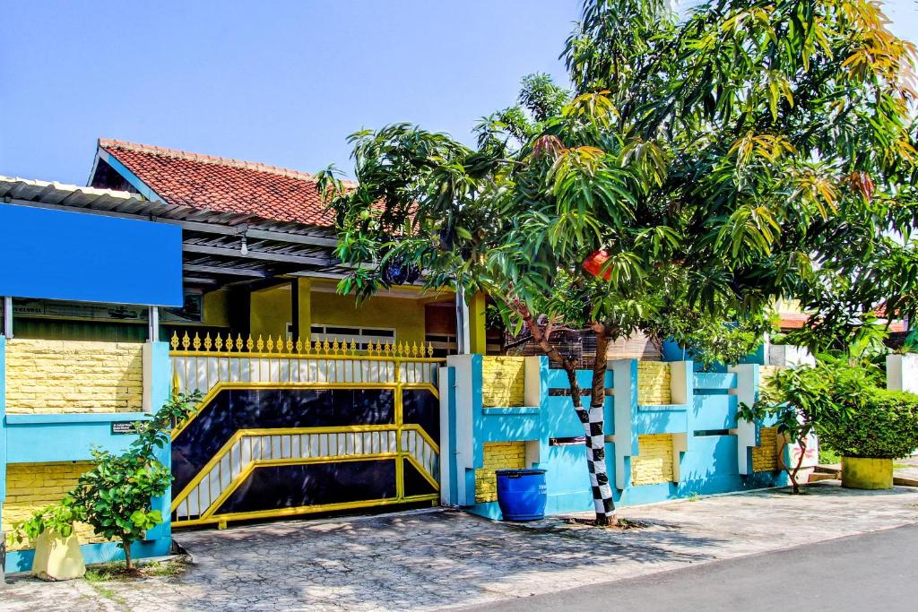 a blue building with a yellow gate and a tree at Hotel O Lobak Hostel CapsuleNearAyam Goreng Terowongan in Alastuwo