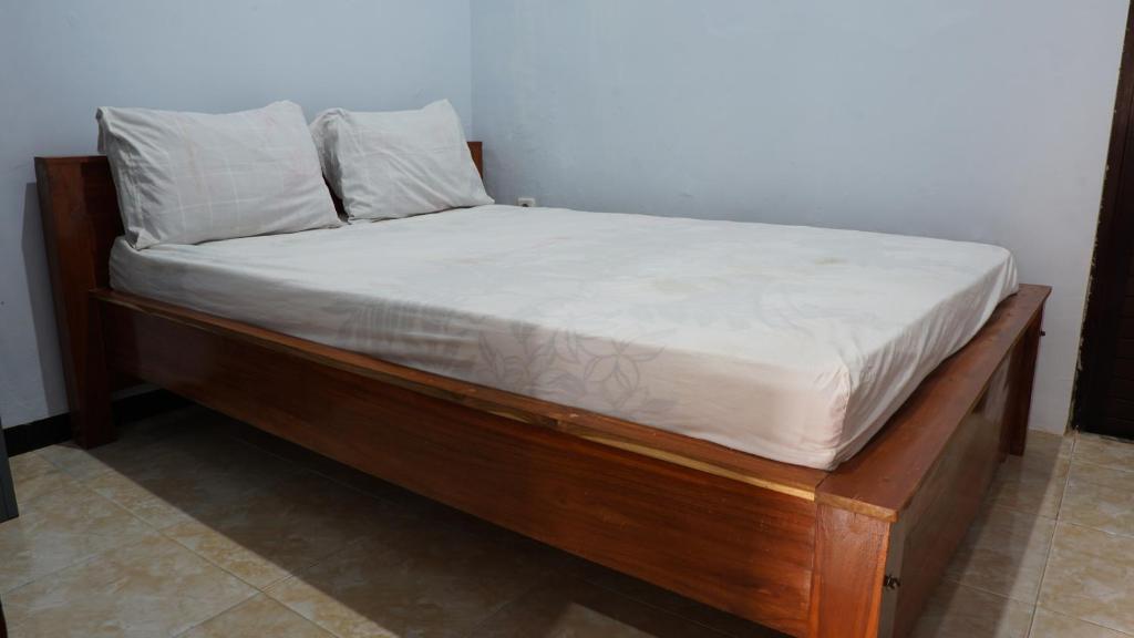 a wooden bed with white sheets and pillows on it at Hotel O Coconut Island Homestay & ResortNearPantai Pulau Merah in Pasanggaran