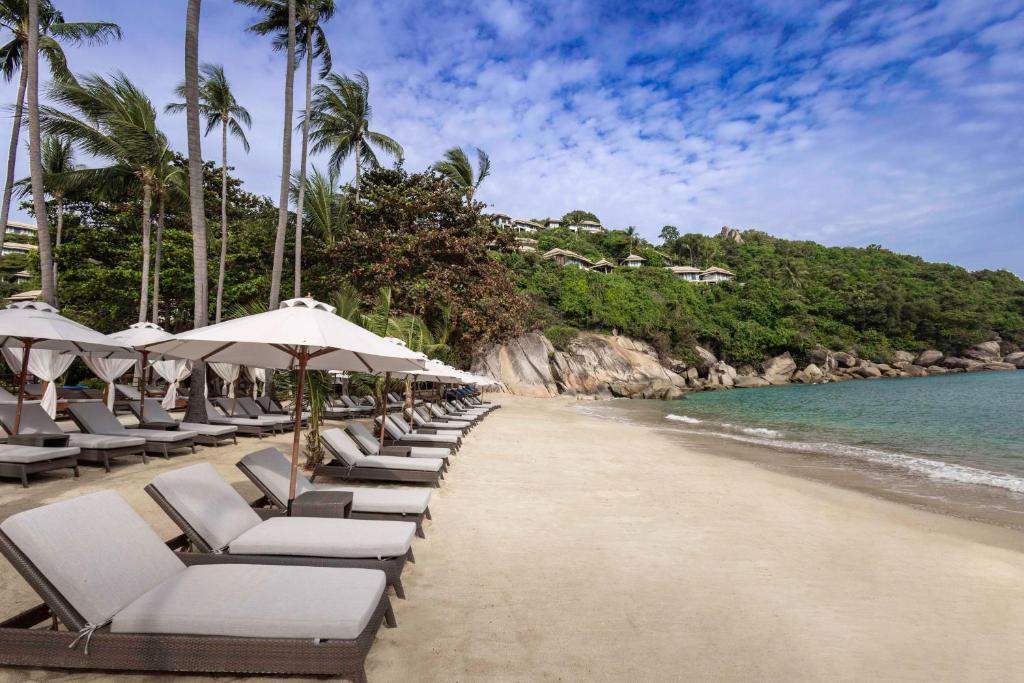 a row of lounge chairs on a beach with the ocean at Banyan Tree Samui in Lamai