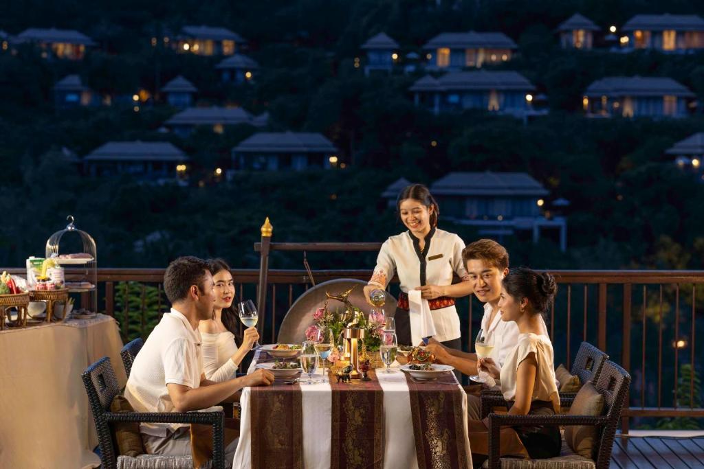 a group of people sitting at a table with a waiter at Banyan Tree Samui in Lamai