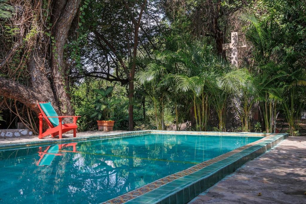 a blue swimming pool with a red chair and trees at Casa Soñada a la Orilla del Rio in Conca