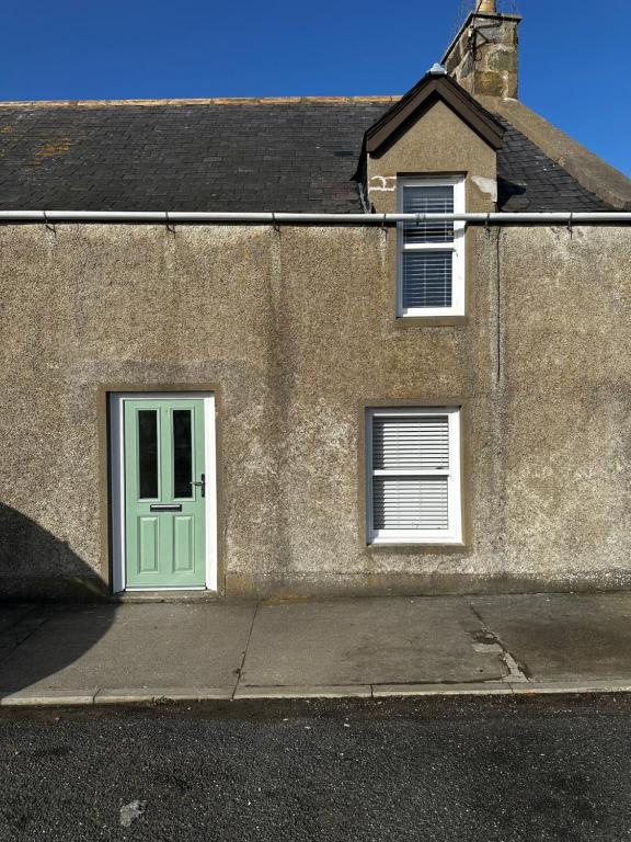 a building with a green door and two windows at Cozy Cottage Retreat in Portsoy