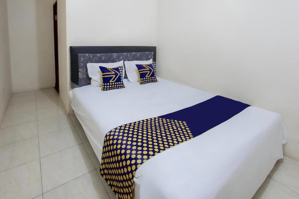 - un lit blanc avec des draps et des oreillers bleus et jaunes dans l'établissement SPOT ON 93724 Songgong Homestay, à Kuta Lombok