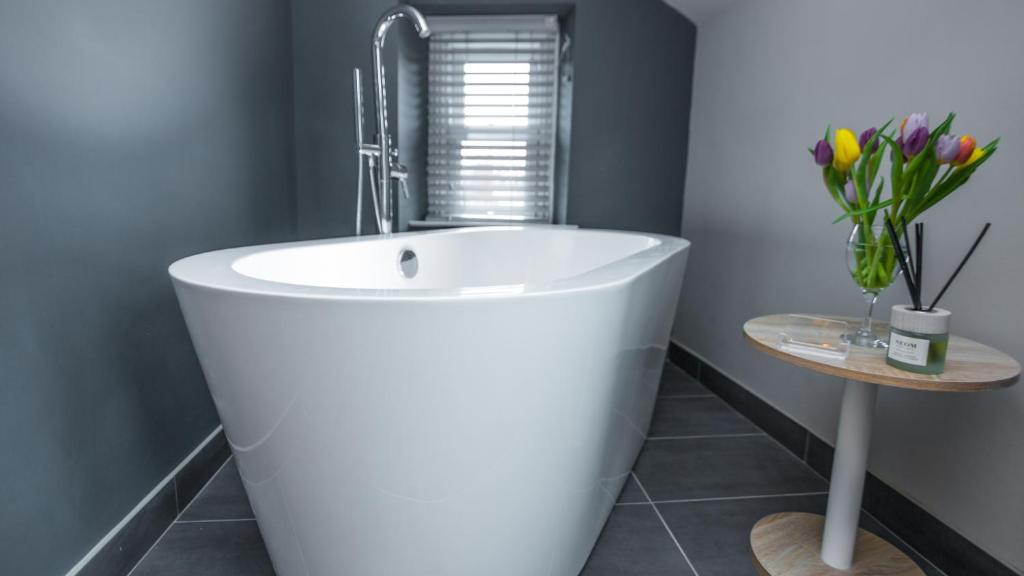 a white bath tub in a bathroom with a table at St Valery Boutique Bed + Breakfast in Alnmouth